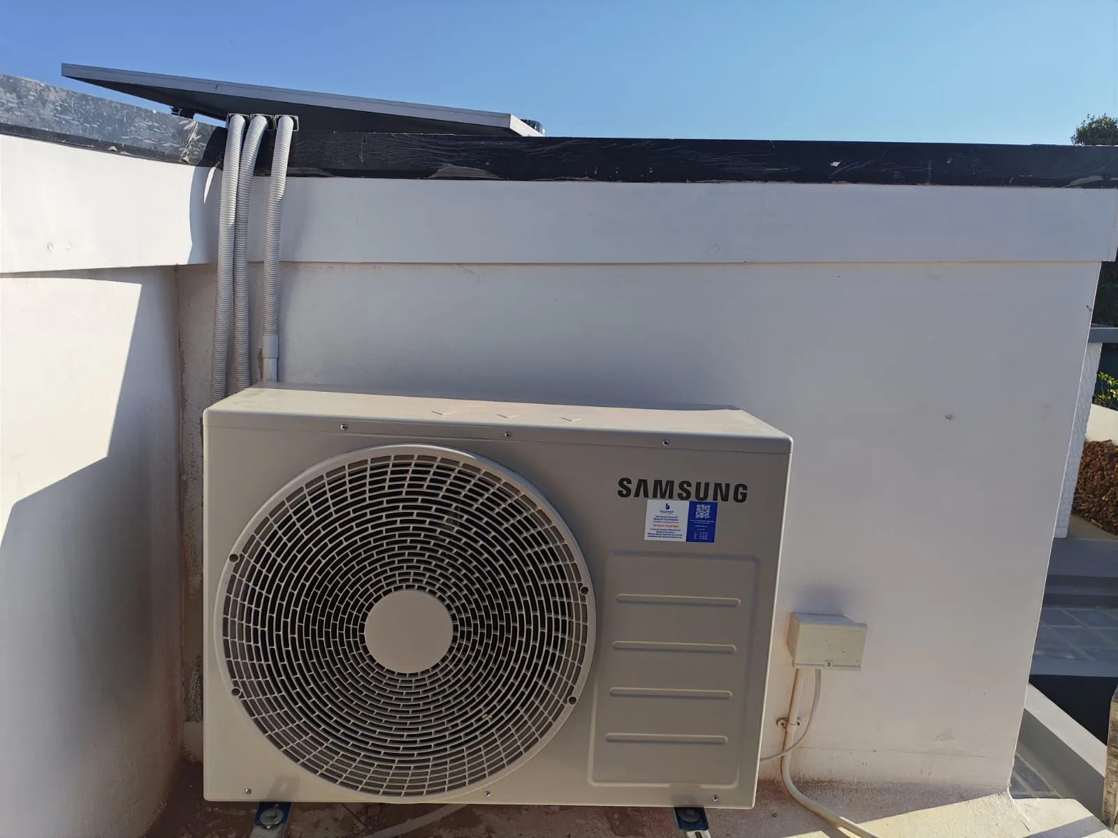 Outdoor condenser installation with insulated pipework routed over a flat roof.