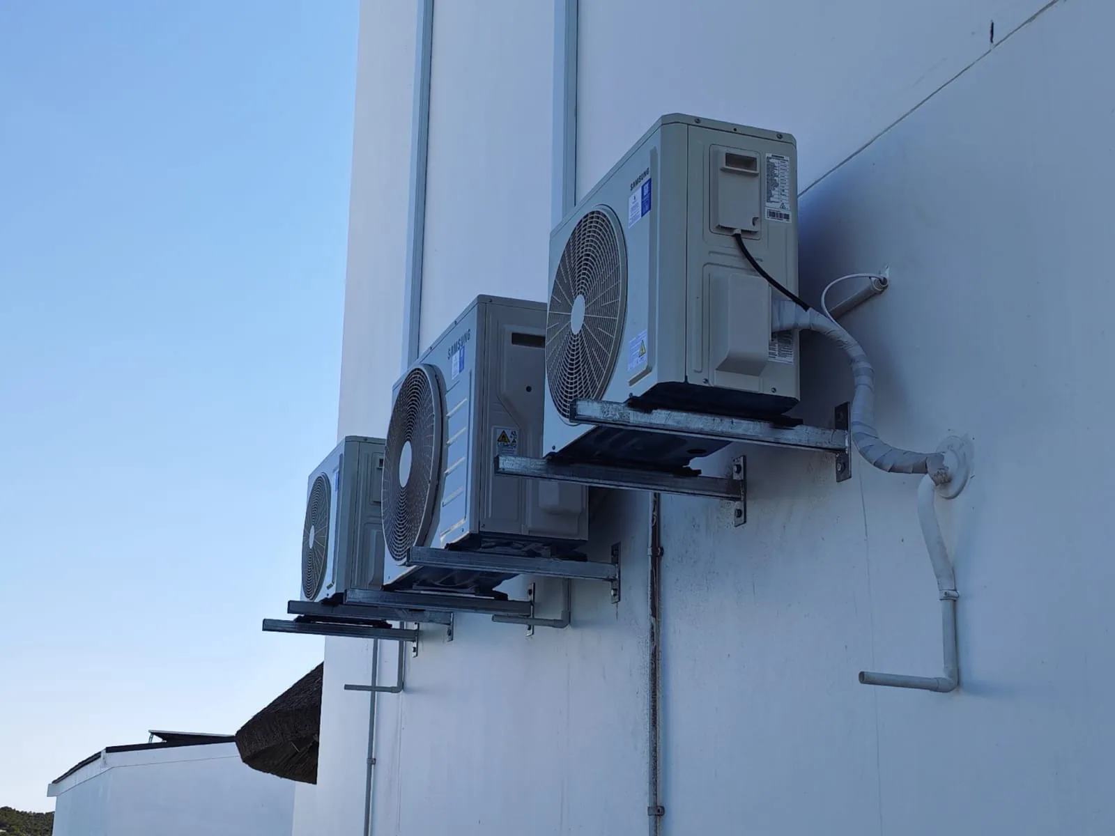Three outdoor condenser units aligned on raised wall brackets.