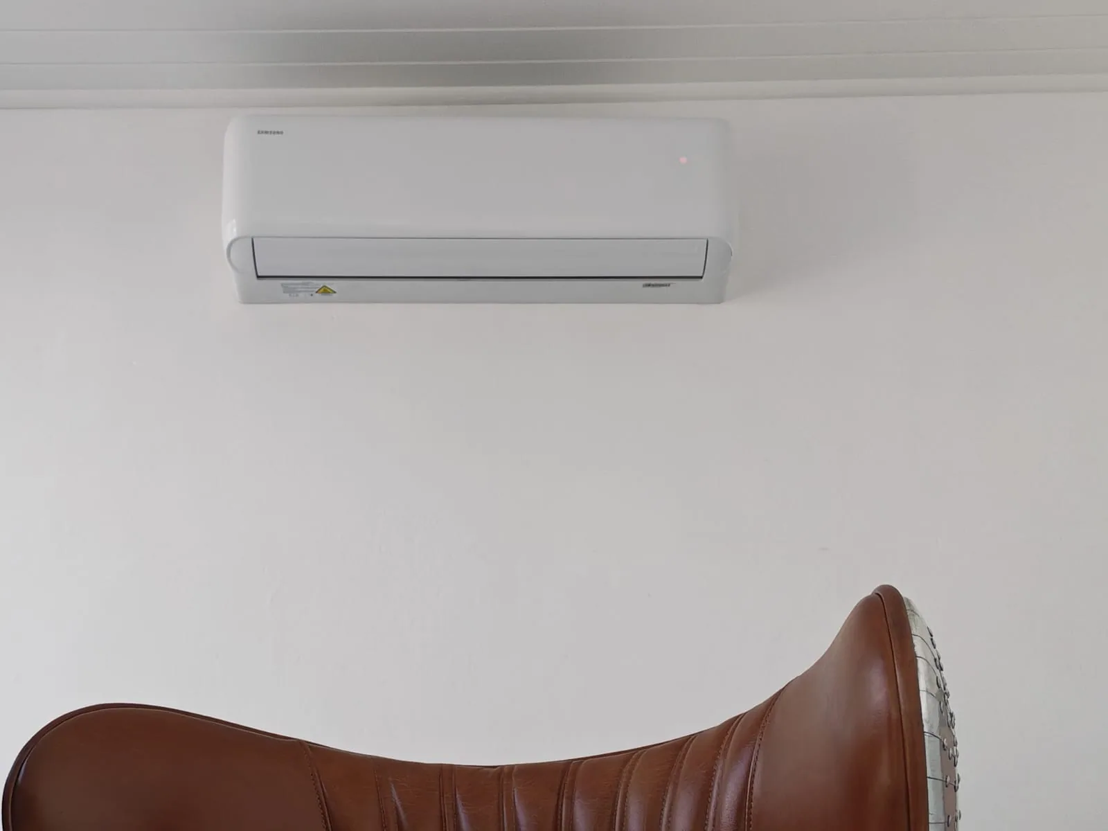Wall-mounted indoor air-conditioning unit above a furnished living area.