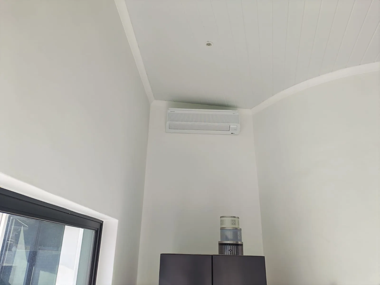 Indoor air-conditioning unit positioned near a window and high ceiling.