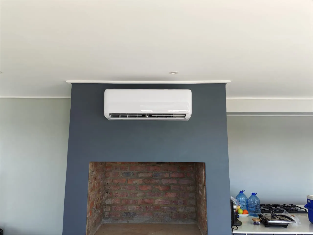 Wall-mounted split air-conditioning unit installed above a brick fireplace.