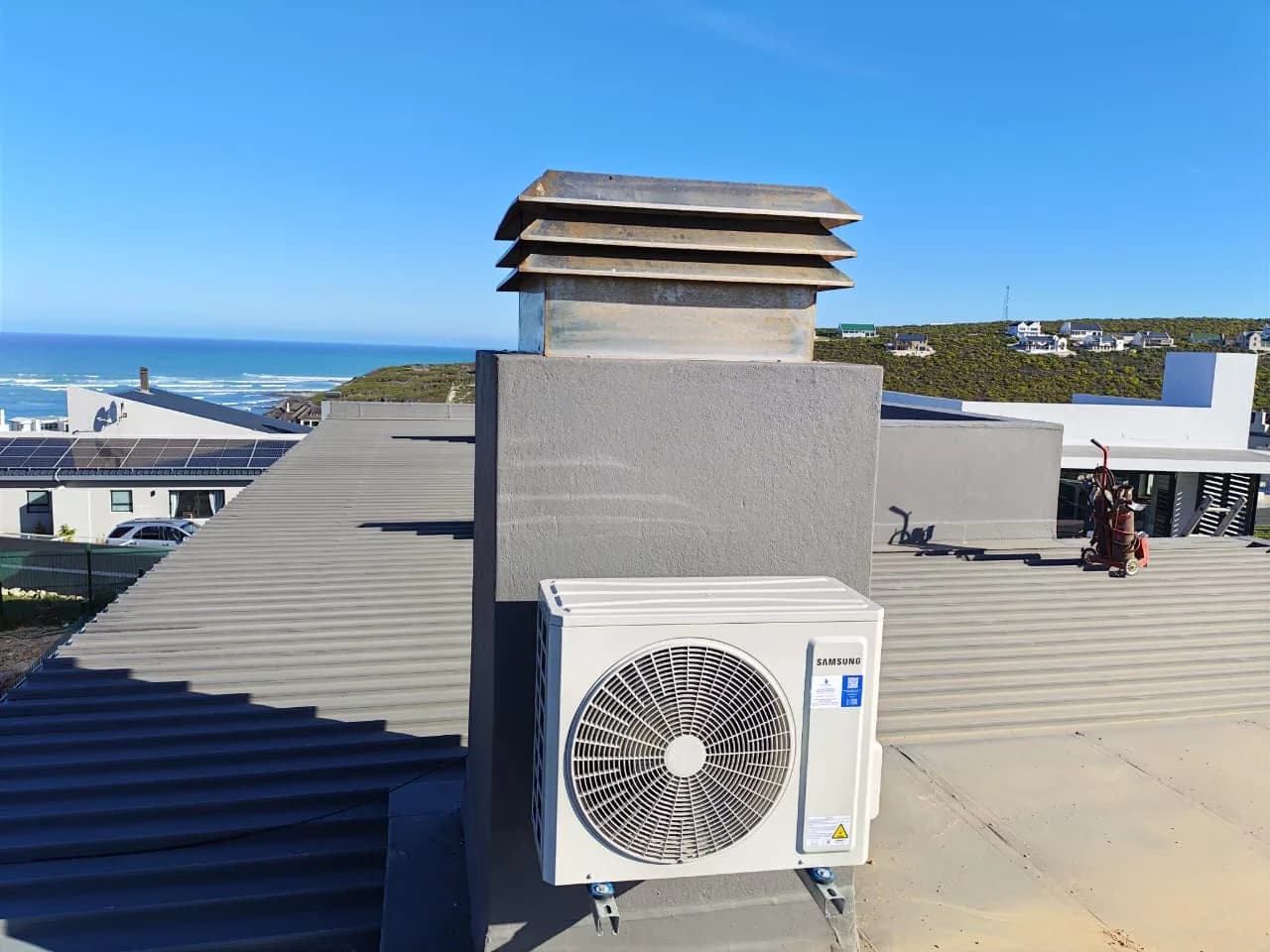 Rooftop condenser installation with surrounding coastal buildings visible.