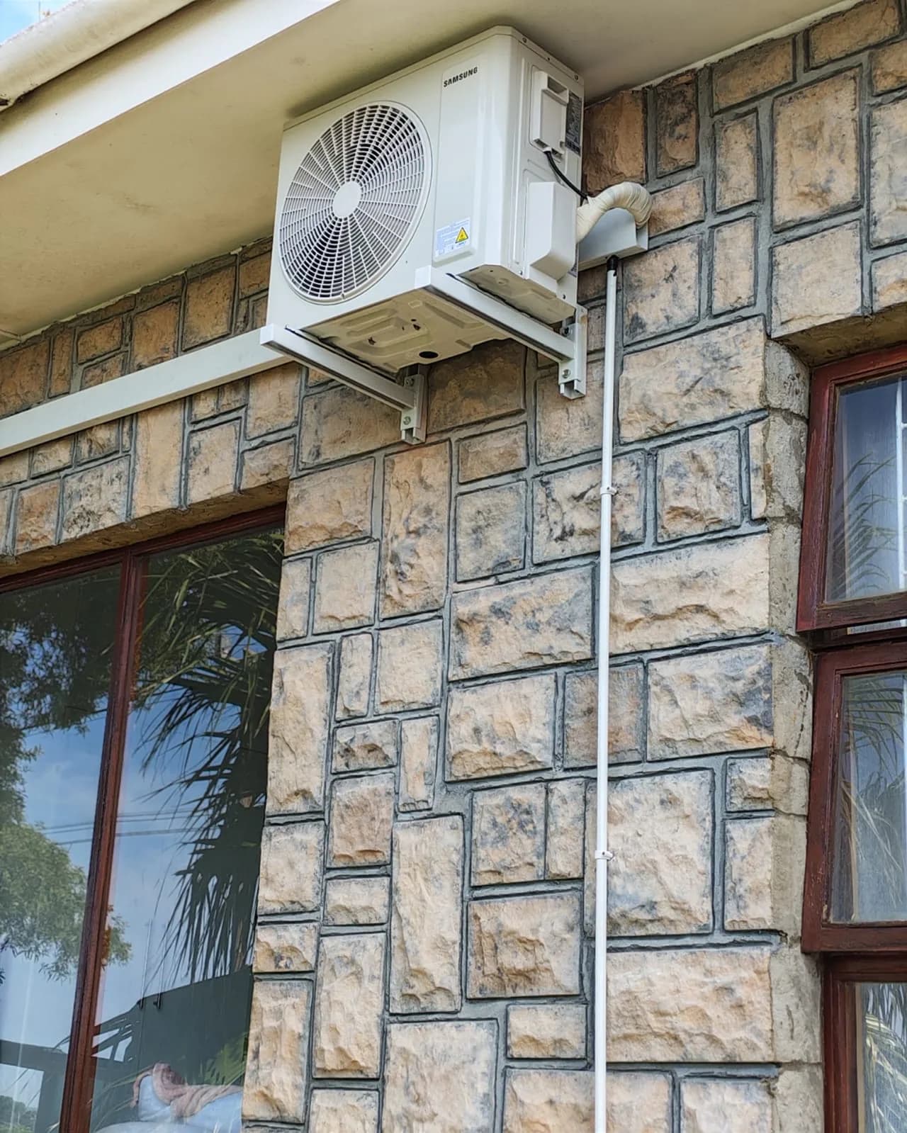 Outdoor condenser and enclosed pipework mounted on a stone exterior wall.