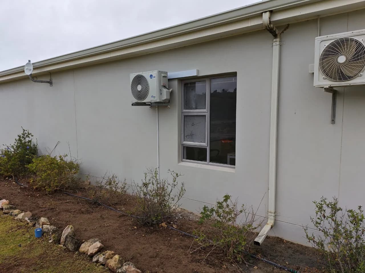 Outdoor air-conditioning condenser mounted beside a window on an exterior wall.