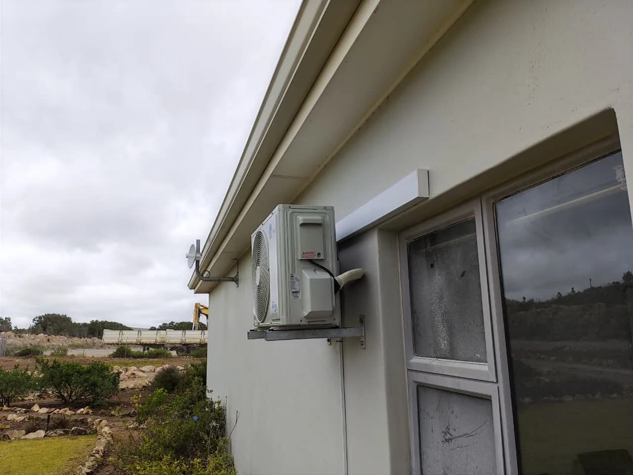 Side view of an outdoor air-conditioning condenser mounted beside a window.